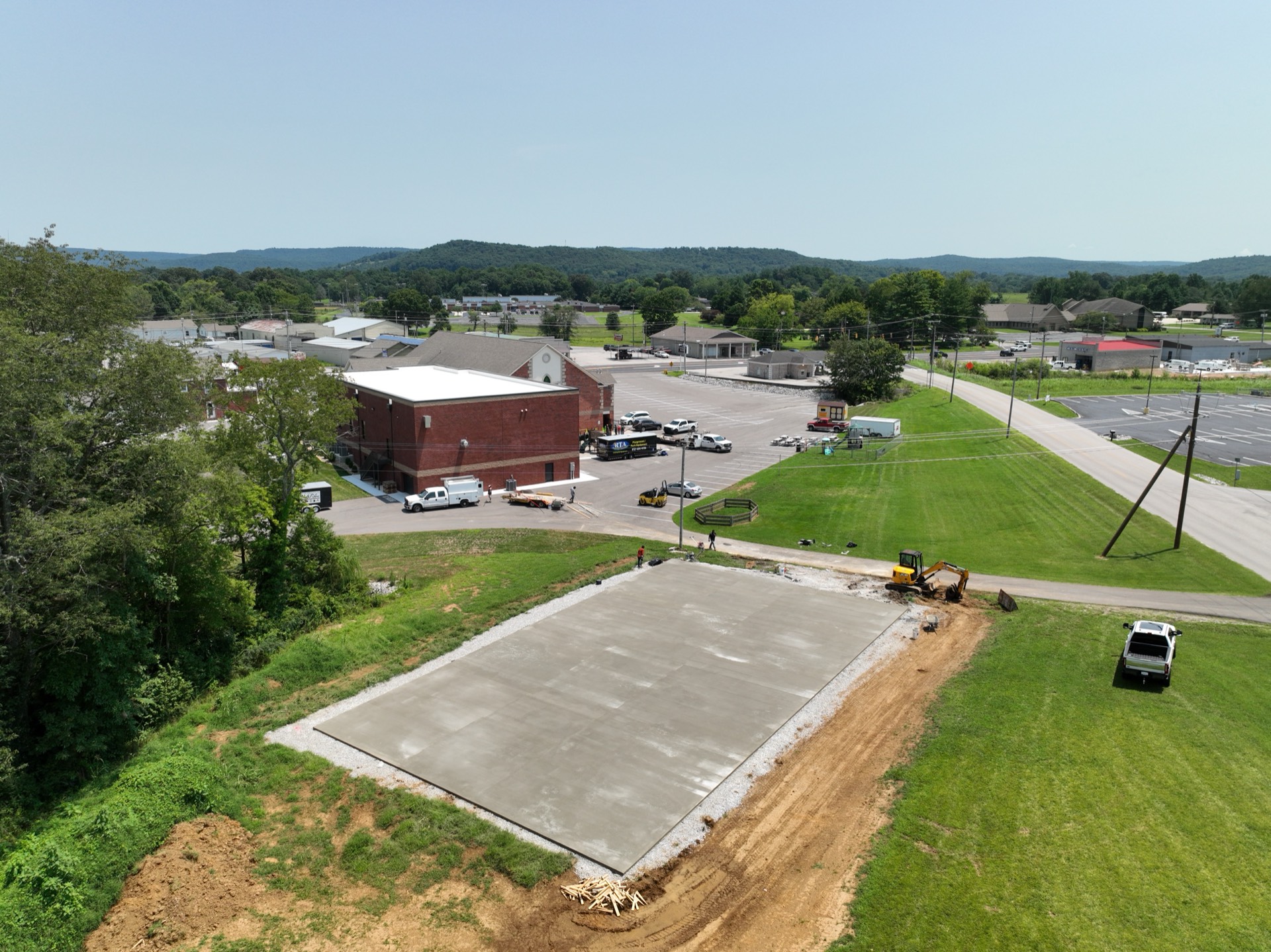 Aerial view of a large fresh concrete slab and site work beside a church parking lot