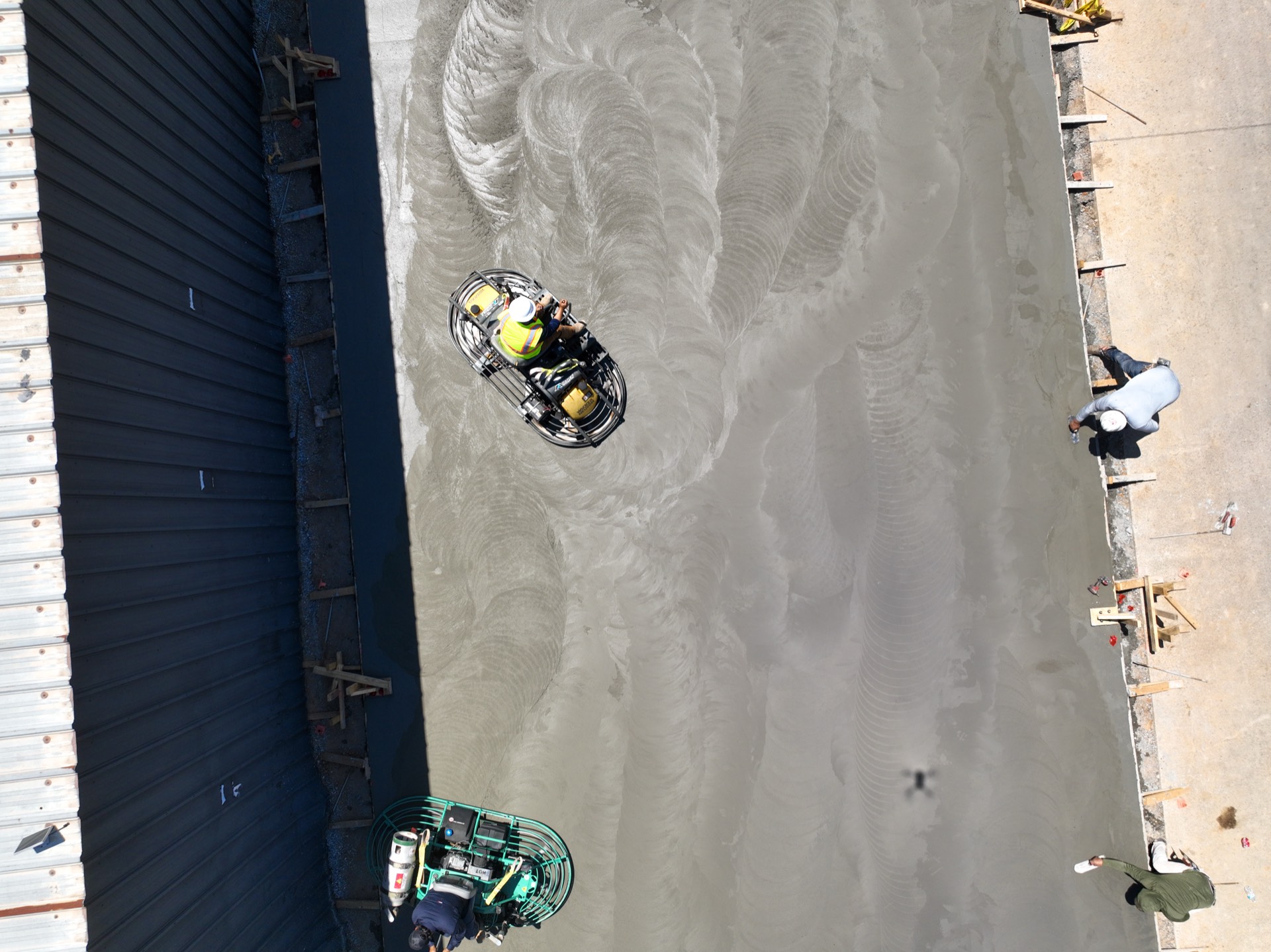 Overhead view of ride-on power trowels burnishing a fresh concrete slab